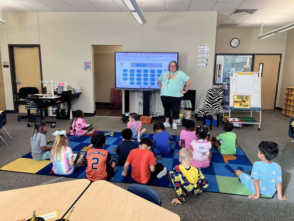 Kindergarten teacher leading class instruction in front of students sitting on the carpet
