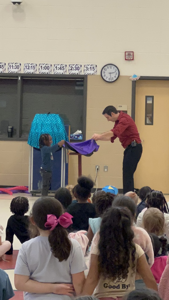 Magician performing trick in front of students while another student assists with sheet
