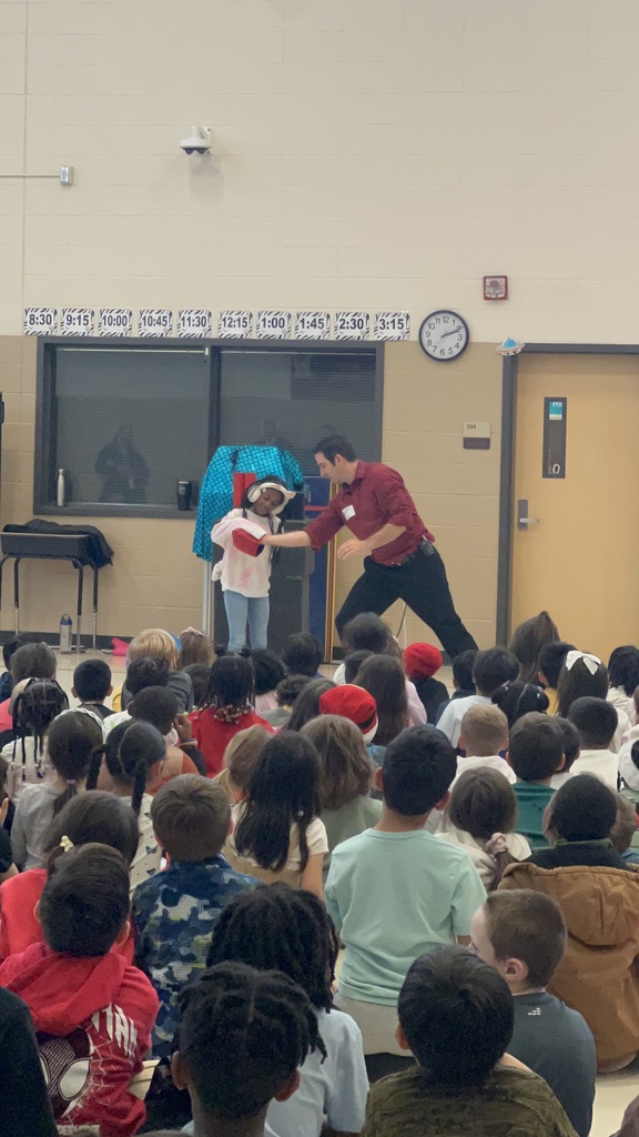 Magician performing trick in front of students while another student stands at the front of the crowd