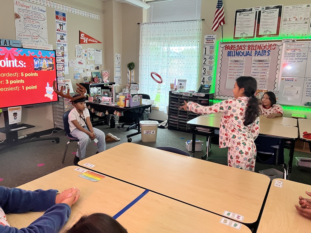 One student is tossing a ring at another student who sits in a chair with reindeer antlers on