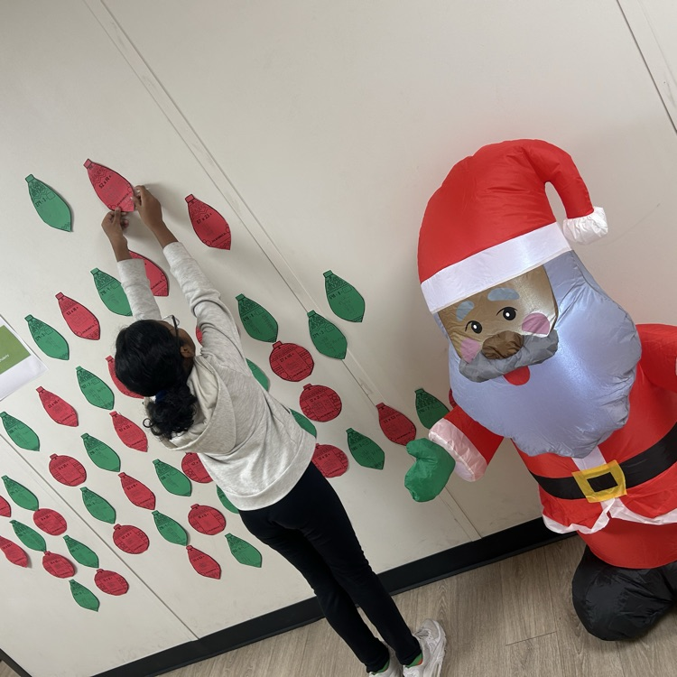 female student standing in front of green and red bulbs for multiplication and division - next to Santa Claus in a red suit 