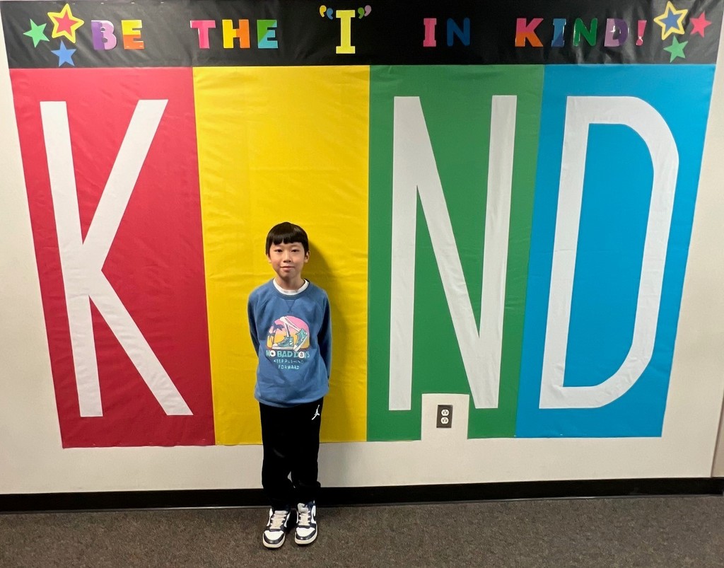 student posing inside the KIND sign as the "i"