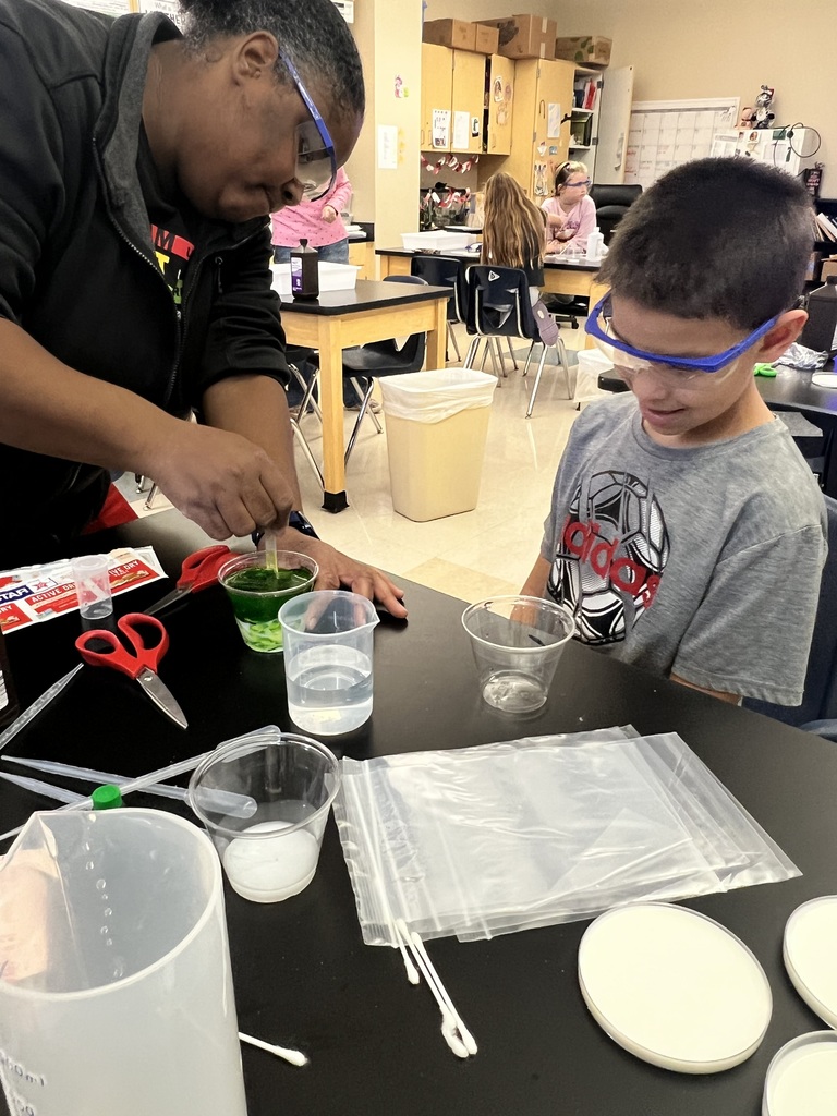 Male student is watching a female teacher stir a substance in a science lab