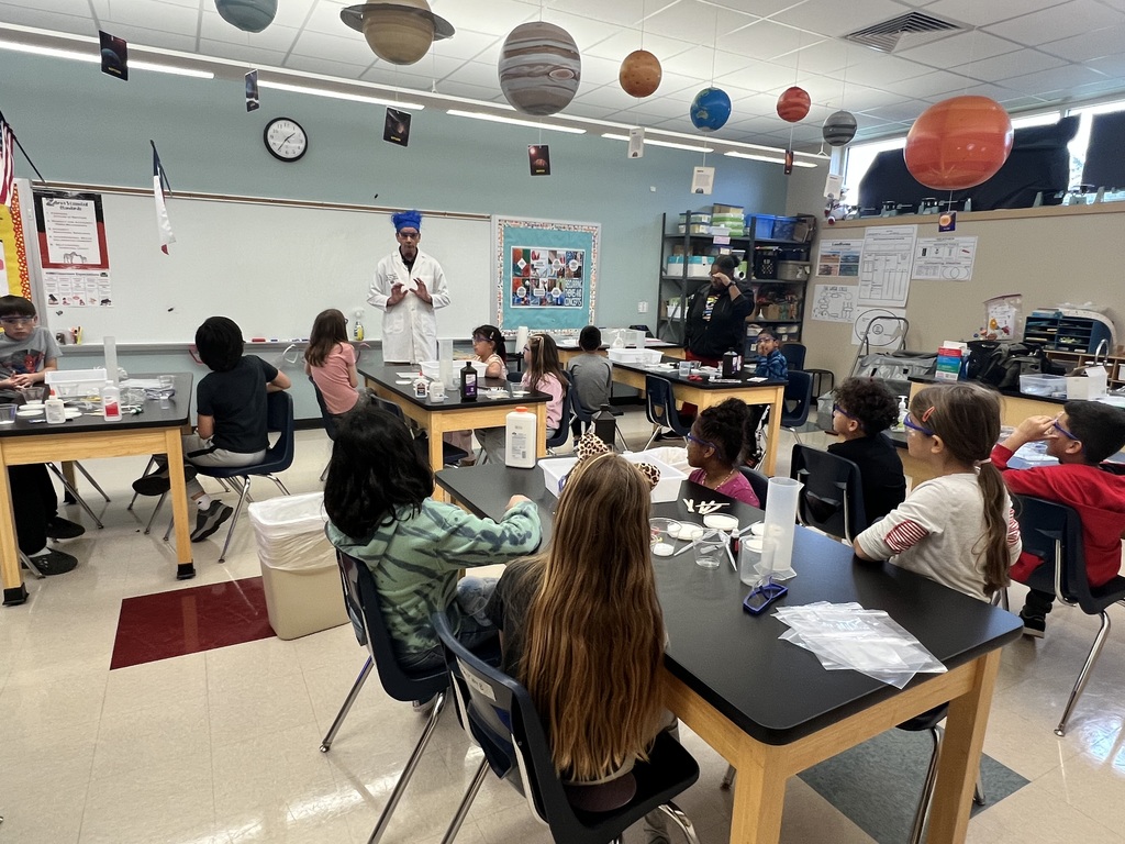 Students sitting at desks listening to a teacher dressed like a mad scientist
