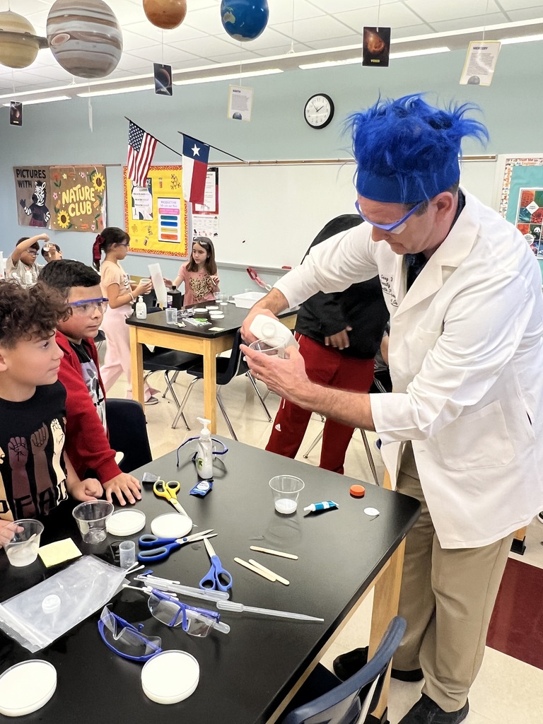 Man in lab coat and blue wig demonstrating a science experiment for students