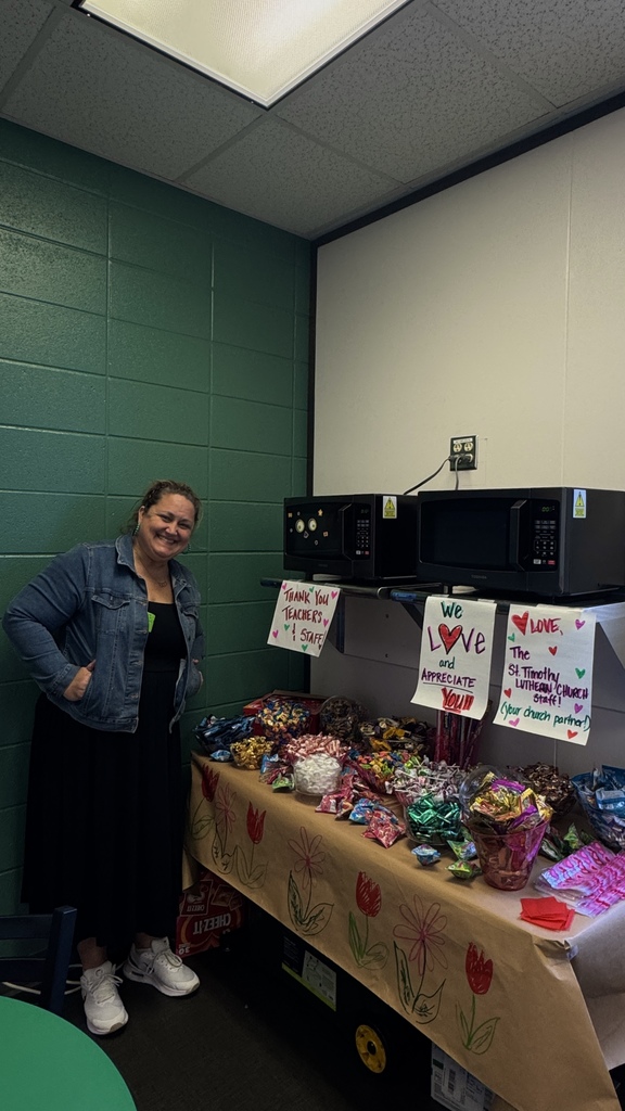 Women standing near table filled with goodies for teachers to fill baggies.