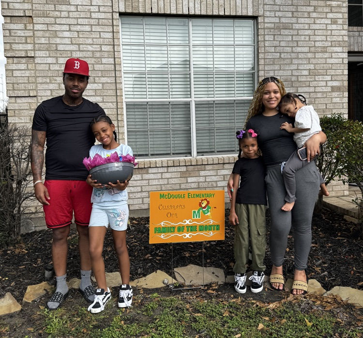 A family standing together with the family of the month yard sign. 