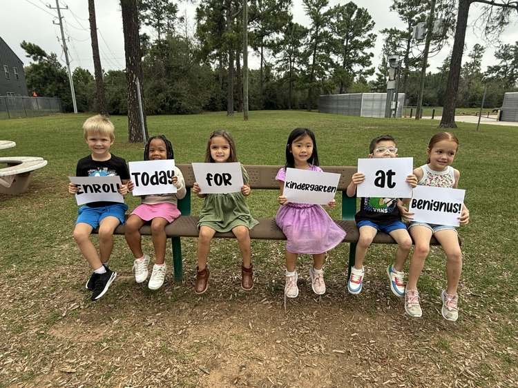 students holding signs that say Enroll today for kindergarten at Benignus