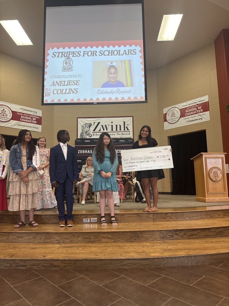 Graduating Senior holding the large check presented to her while 5th grade students look on