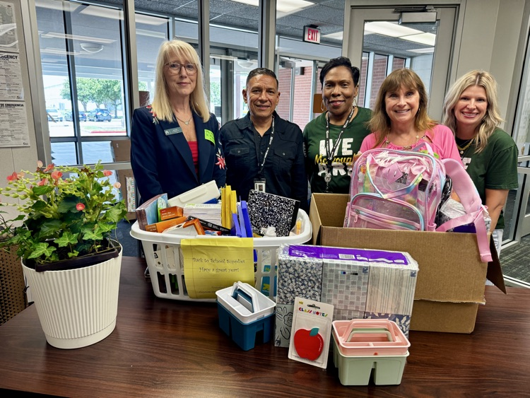 A group of people standing behind the counter with school supplies. 