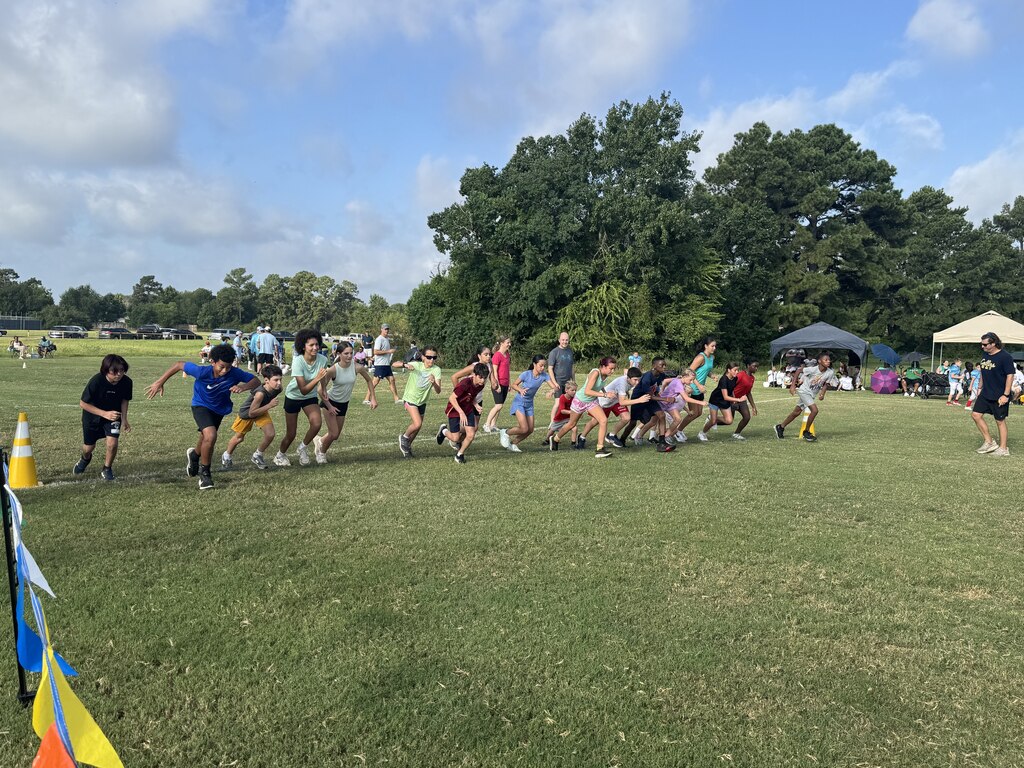 People run in a field with flags and orange cones, surrounded by trees and tents.