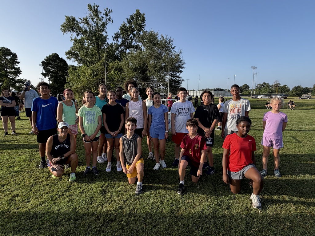 Group of young people in sports attire poses on a grassy field with trees in the background.