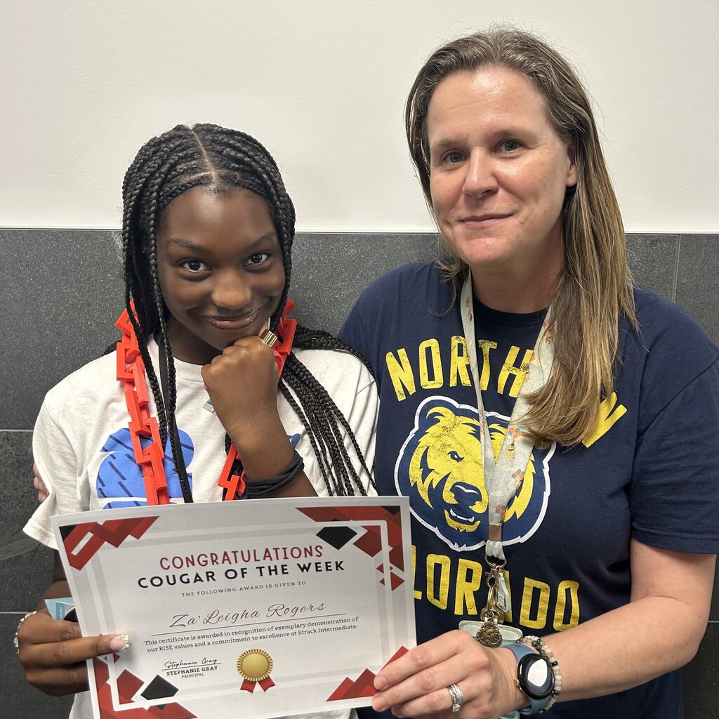 A young person holds a certificate while posing with a woman in a blue shirt.