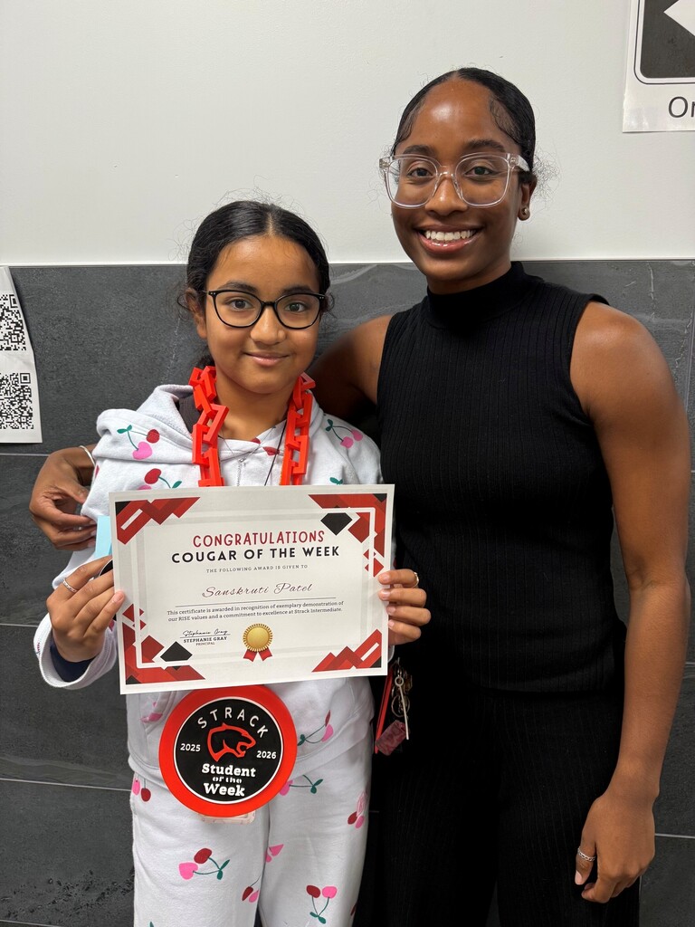 A girl in white pajamas holds a certificate and stands next to a smiling woman in black.