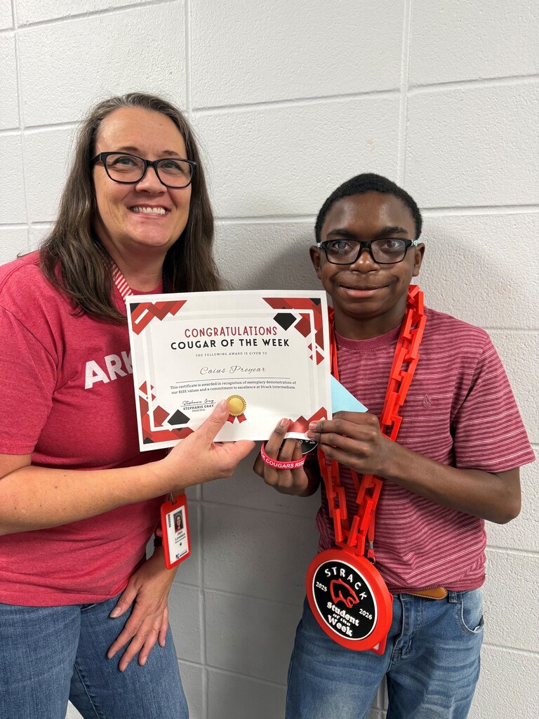 A woman in a red shirt holds a certificate while standing next to a boy wearing glasses and red necklaces.