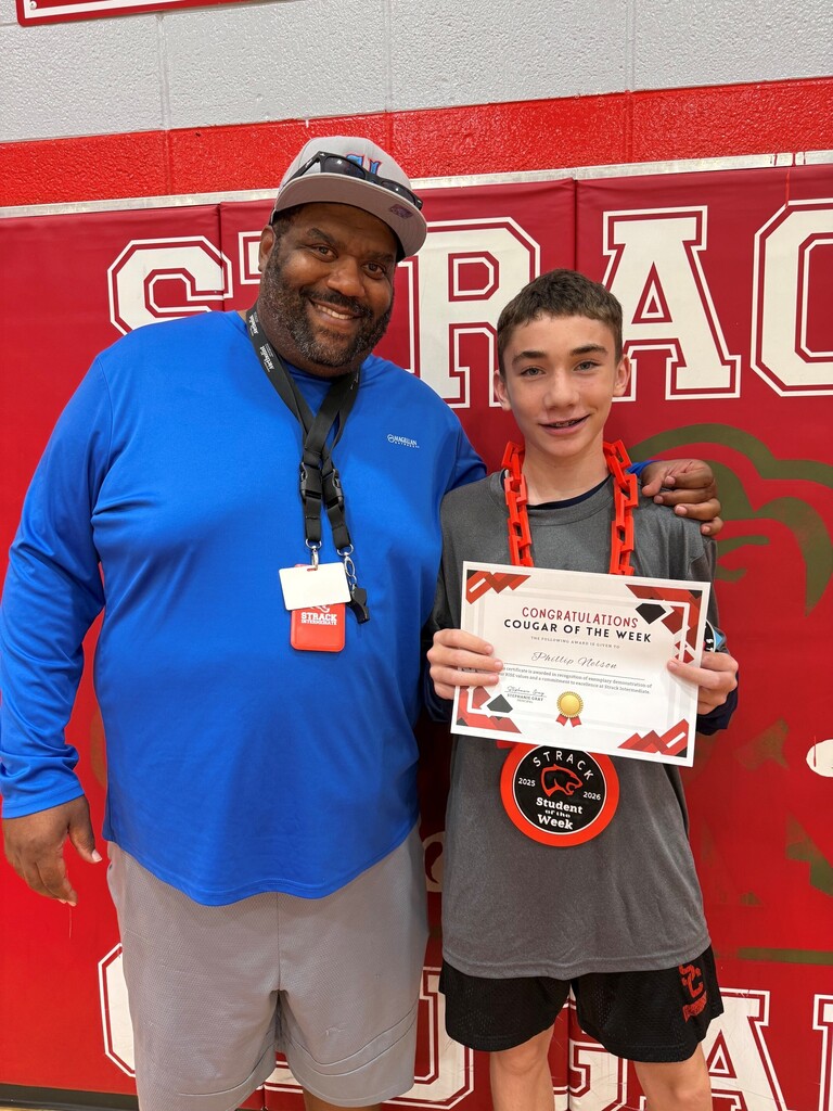 A man in a blue shirt and a young boy in a gray shirt hold a certificate in front of a red wall with white text.