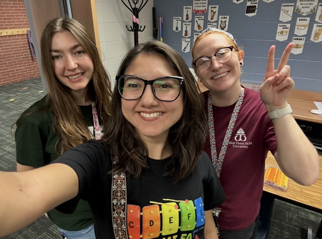 Three women posing with peace signs. One wears a colorful shirt, another a green shirt, and the third a maroon shirt.