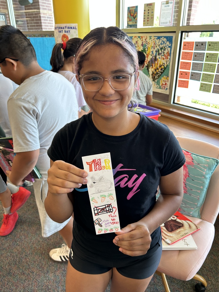 A young girl with glasses holds a ticket while standing in a room with others near a window.