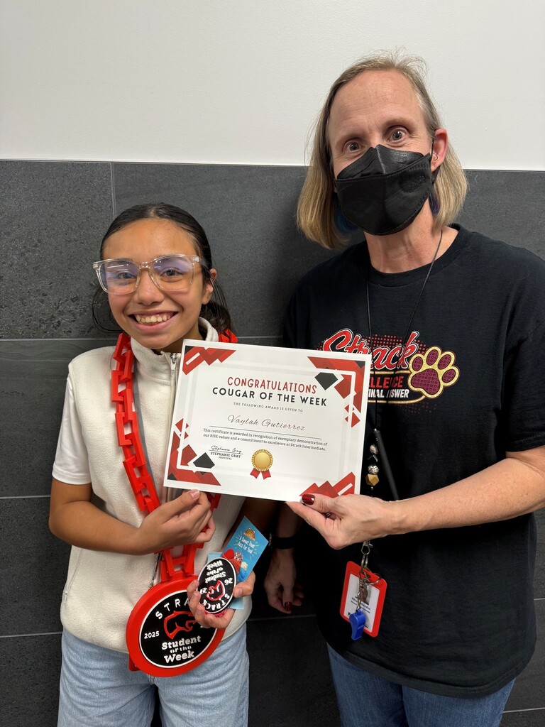 A woman in glasses holds a "Cougar of the Week" award next to a smiling woman in a mask.