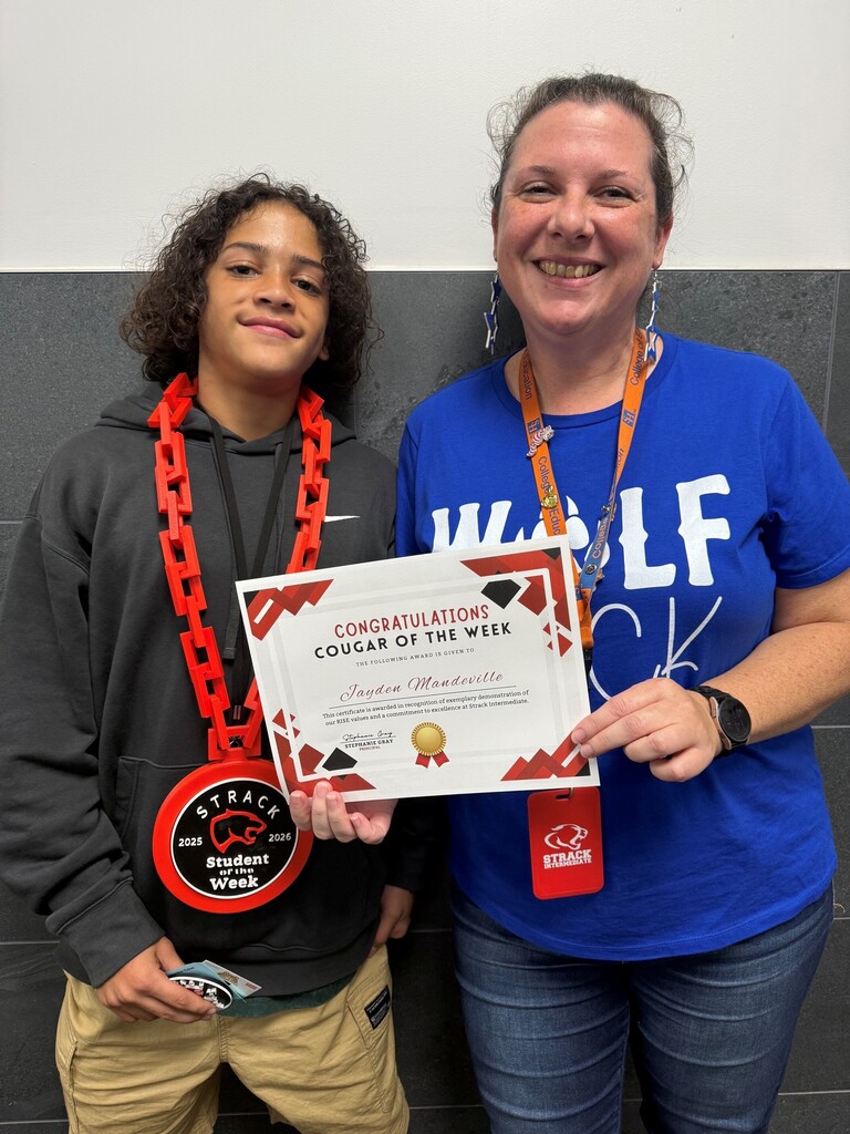 A boy and a woman stand next to each other. The boy holds a certificate for Student of the Week, and the woman wears a lanyard.