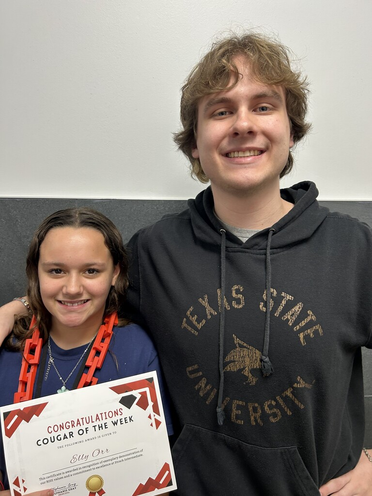 Teen holding certificate with text. Teen wearing black hoodie with "Texas State University" text. Neutral background.