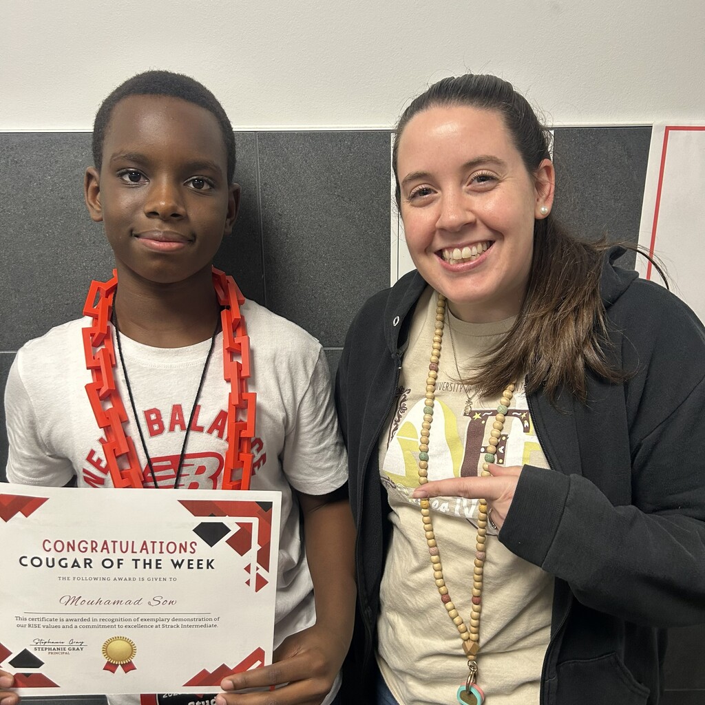 Boy holds a certificate with a woman beside him. Both are smiling. Background is a wall with a geometric pattern.