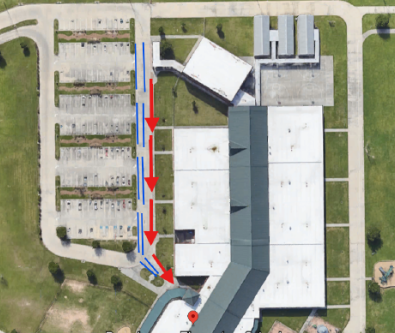 Aerial view of a building with a parking lot. Three red arrows indicate directions. The building has a grey roof.