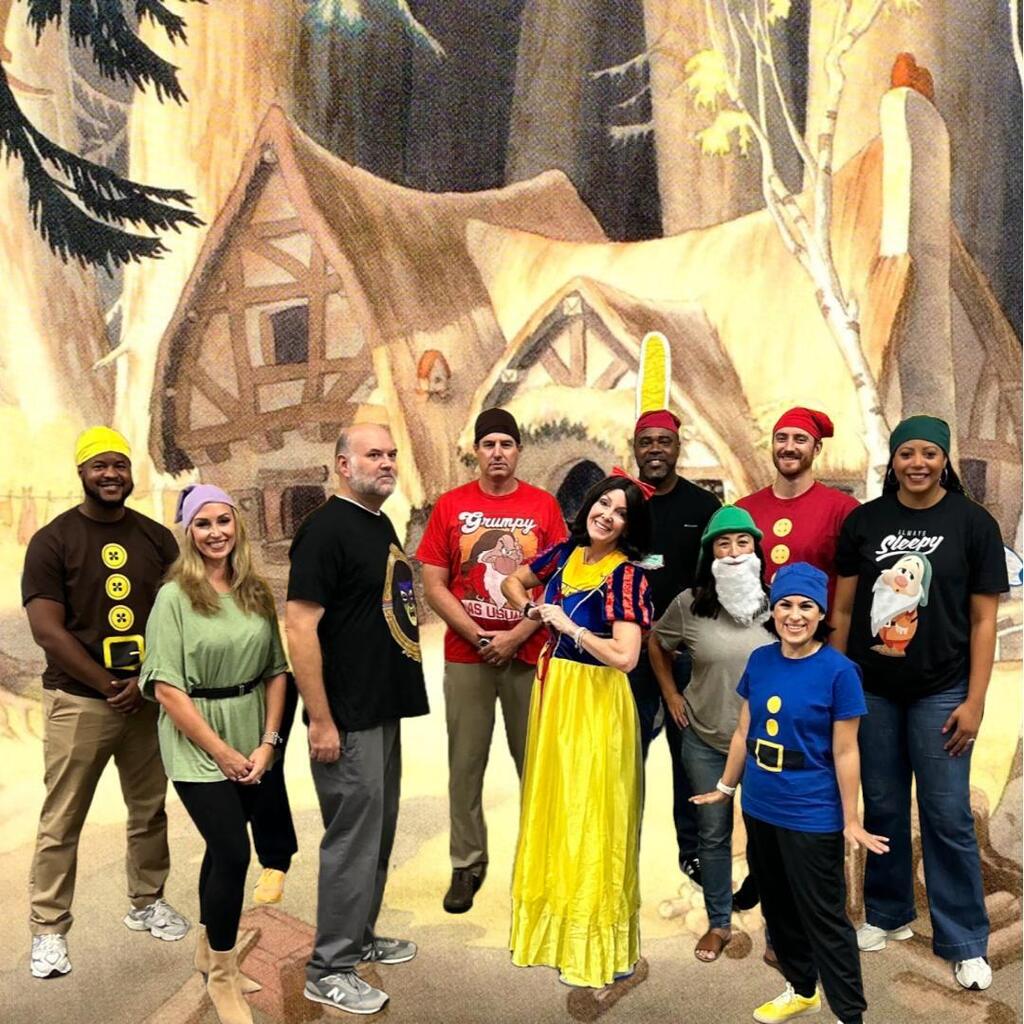 People dressed as Disney characters, including Snow White, stand in front of a painted forest background.