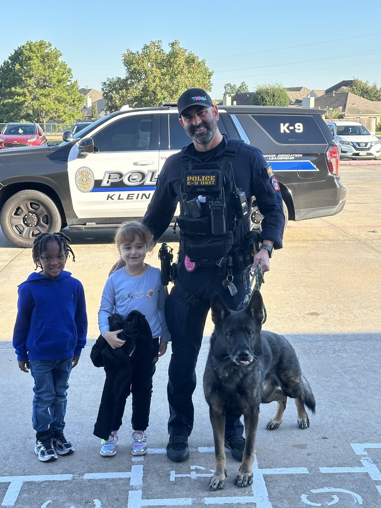Police officer in uniform with a K-9 dog stands with two kids in front of a police SUV.