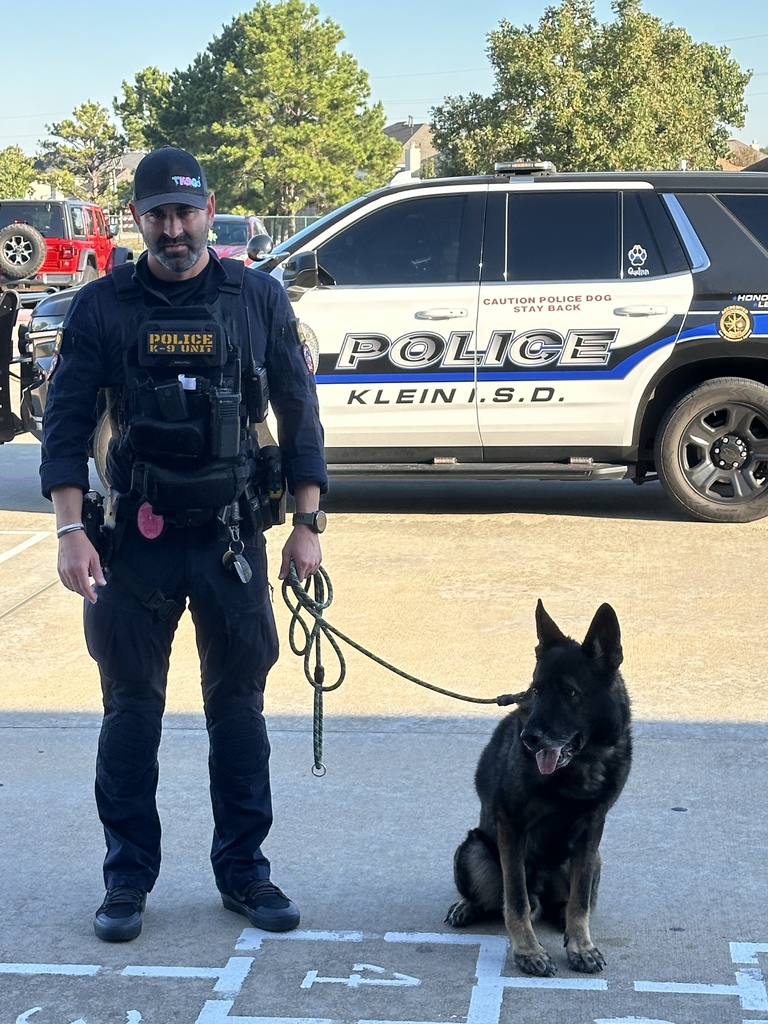 Police officer in uniform walking a German shepherd on a leash on a street.