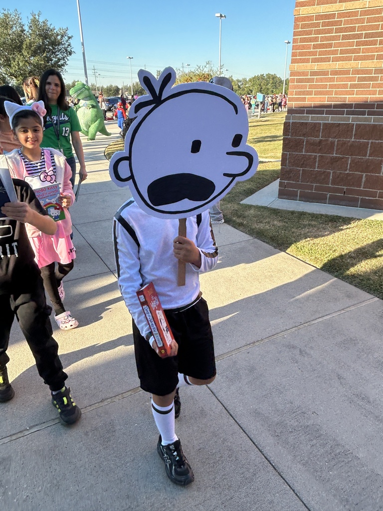 Child wearing a mask of a face holding a book and walking on a sidewalk.