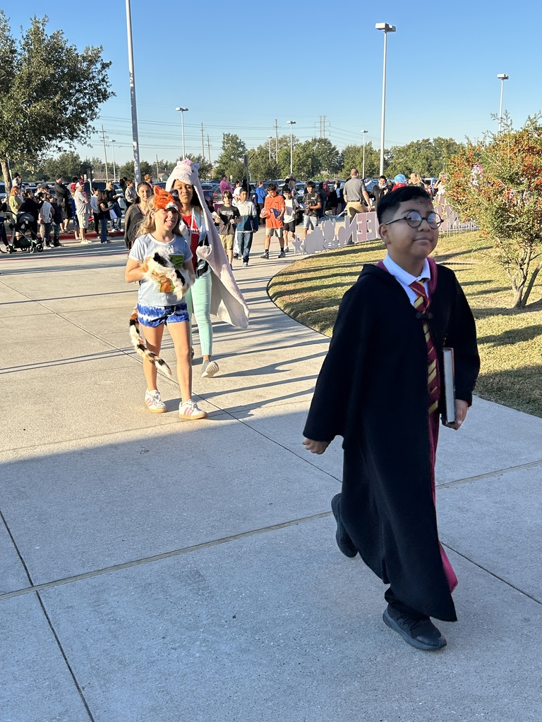A boy and girl in costumes walking on a school sidewalk, with others in the background.