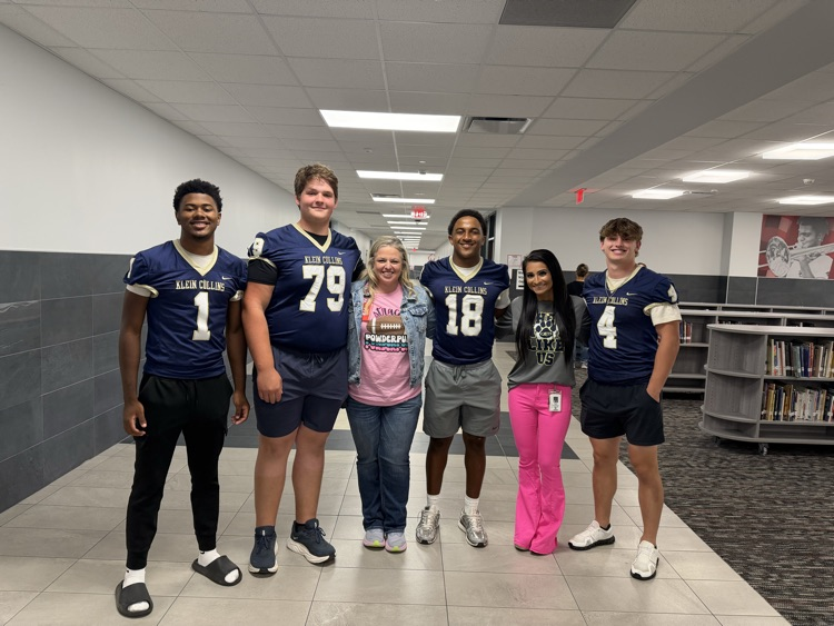 Six people in athletic wear, two women and four men, standing together in a school hallway.