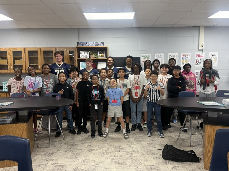Students and staff standing in a classroom; some hold snacks, and others smile and pose for a photo.