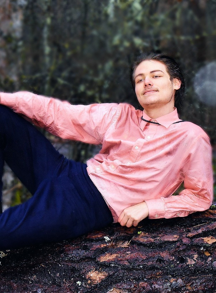 A picture of the Klickitat school student broadcaster, Eann Robinson, laying on a log for their senior photo. Fun fact - the picture was taken by their father.