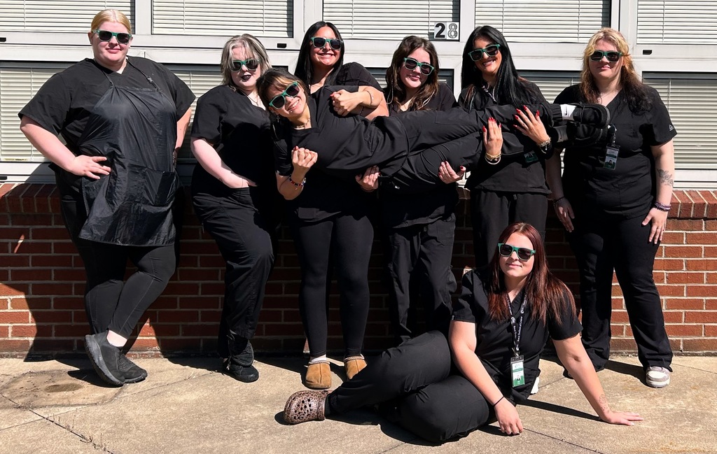 Group photo of 8 Cosmetology students posing, with sunglasses outside.