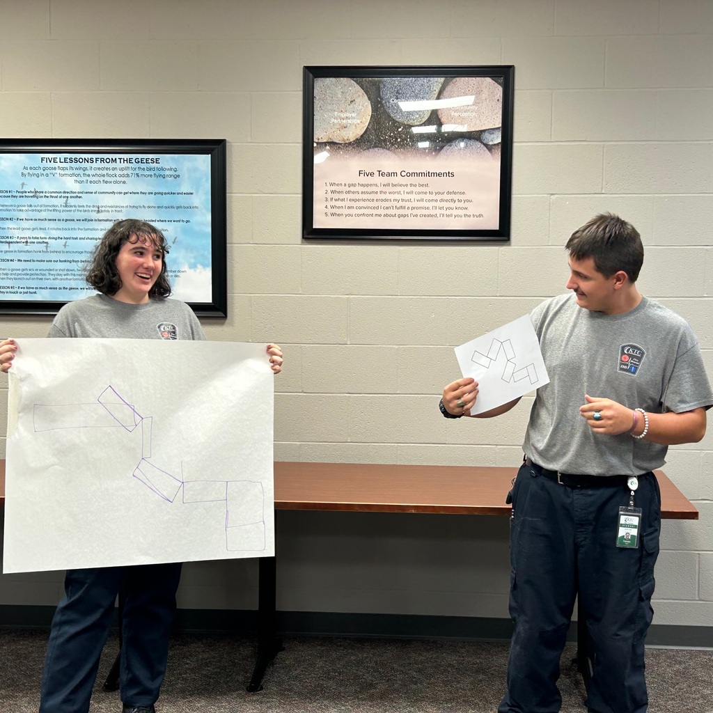 One student holding large paper with drawing and another student holding the original picture to compare
