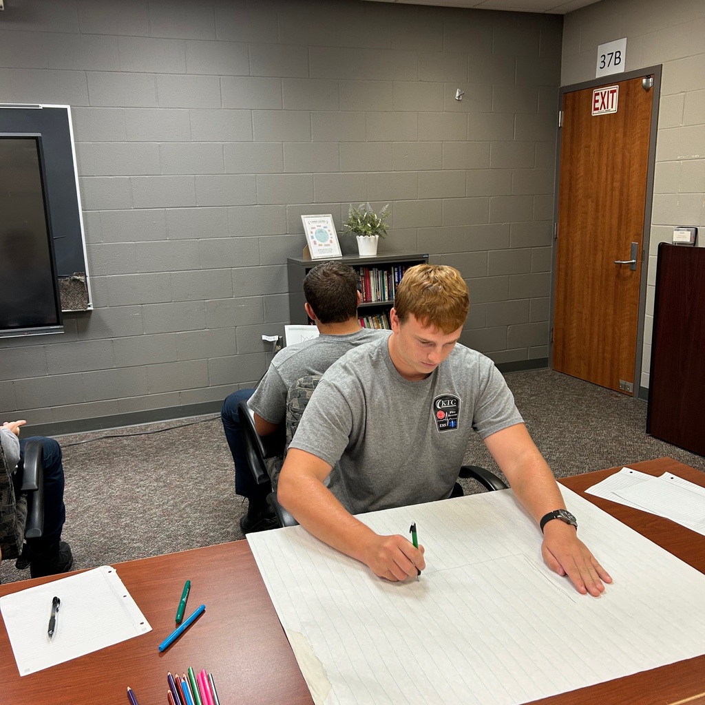 Student drawing on large paper while back to back with another student.