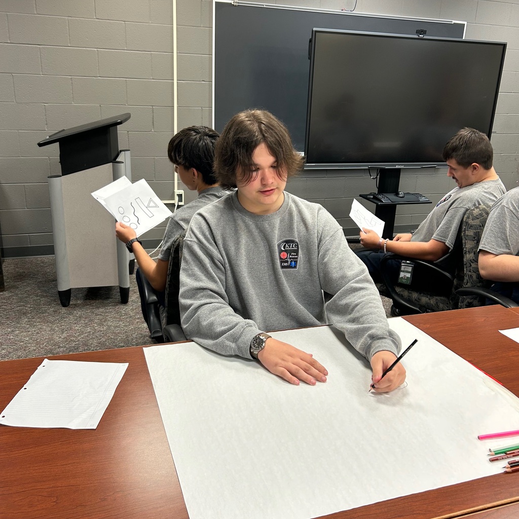 Close up of one student drawing on a large paper while another student is behind him describing the photo