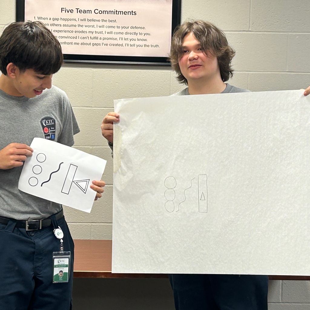 One student holding large paper with drawing and another student holding the original picture to compare