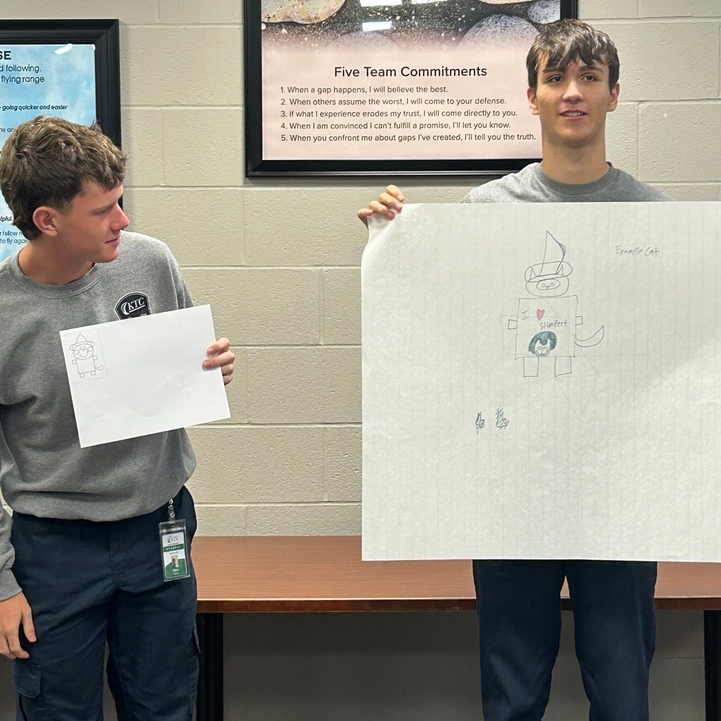 One student holding large paper with drawing and another student holding the original picture to compare