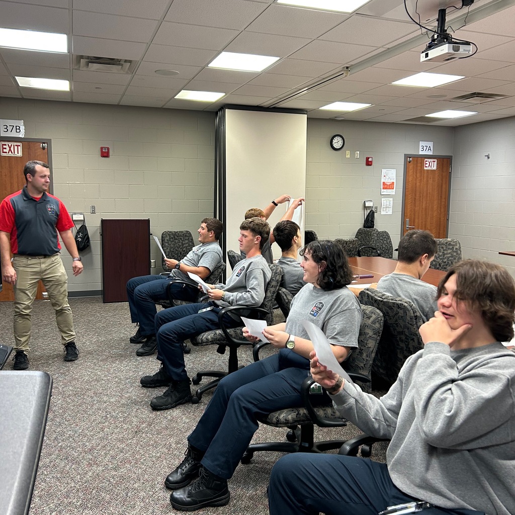 Group of students sitting back to back to their partner and looking at a photo. The instructor is standing in the room.