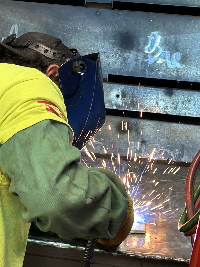 Welding student with helmet down, welding in booth with sparks flying