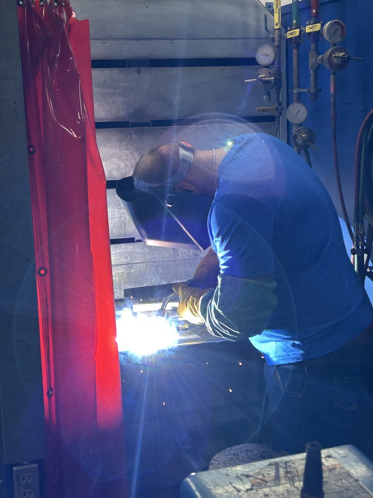 Welding student in booth, with torch, welding material