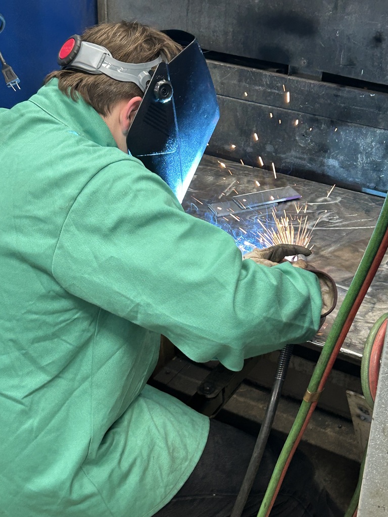Welding student with helmet down, welding in booth with sparks flying