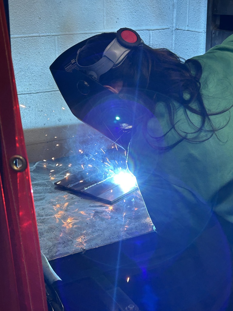 Female welding student welding with helmet down and sparks flying