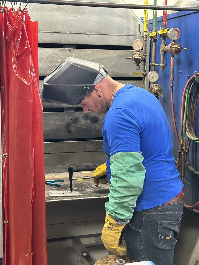 Welding student with helmet up and hammering metal in welding lab