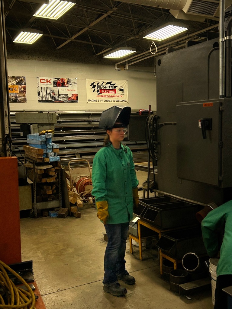 Female welding student standing in welding lab with helmet up and equipment in background