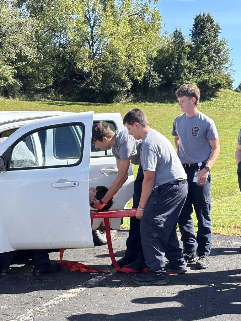 EMS trainees practicing extricating a patient from a white truck using a red spine board.