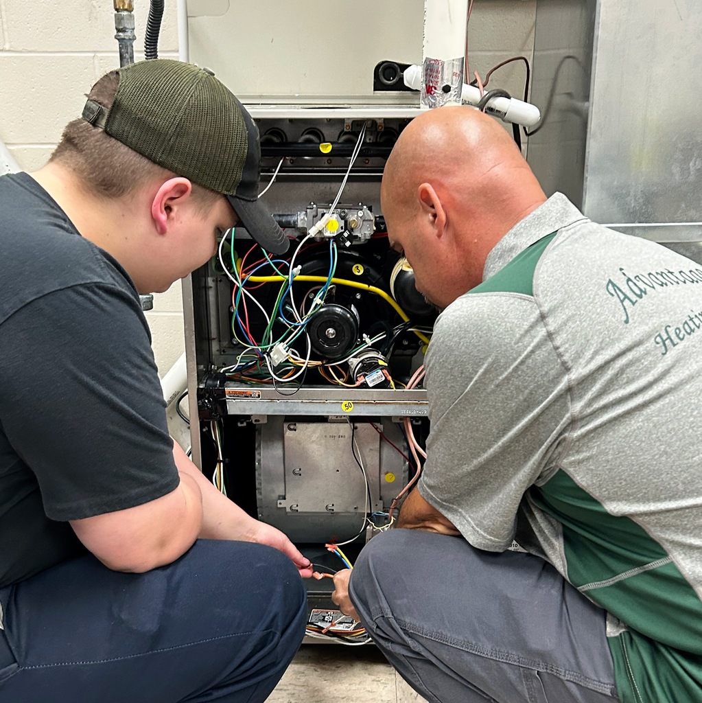 An HVACR instructor guides a student as they examine electrical wiring inside an open furnace unit.
